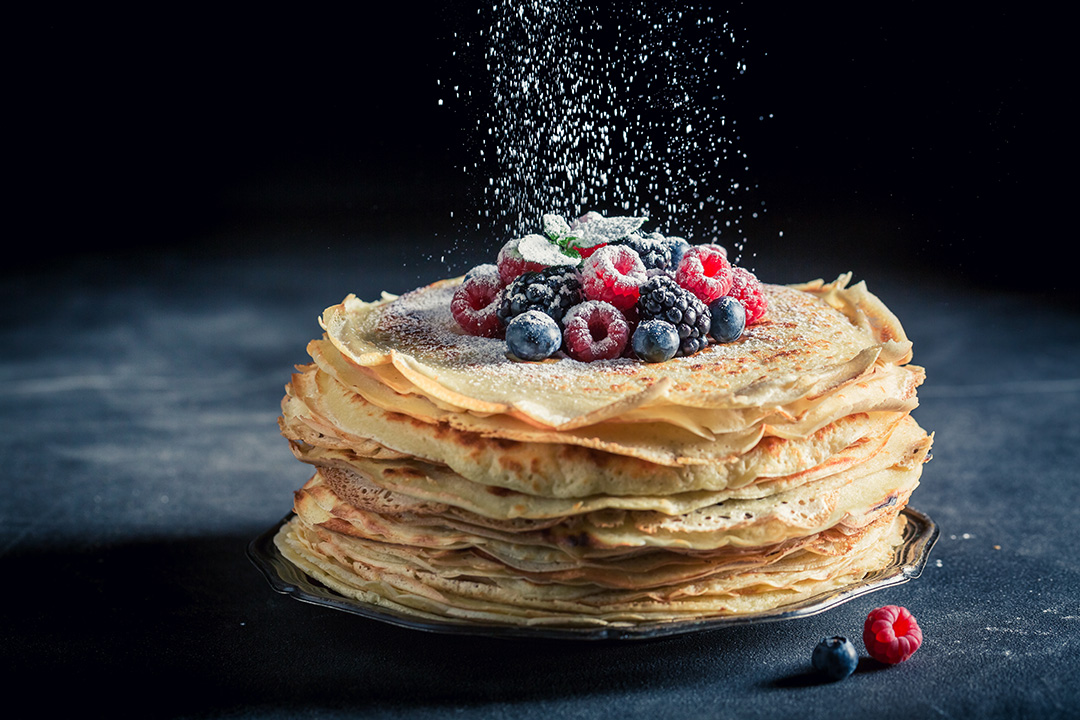 A stack of pancakes topped with berries and icing sugar